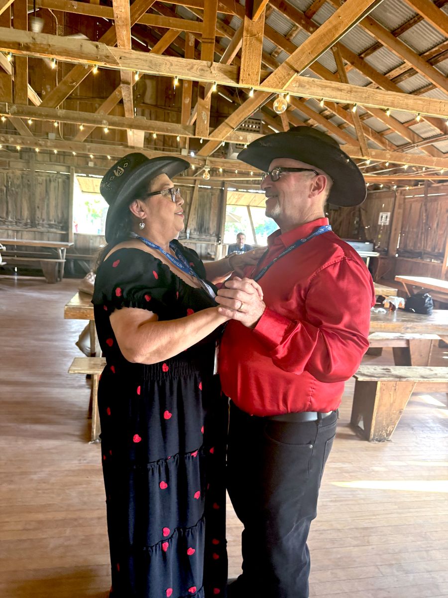 Photo shows a man and a woman dancing together. They are both wearing cowboy hats.