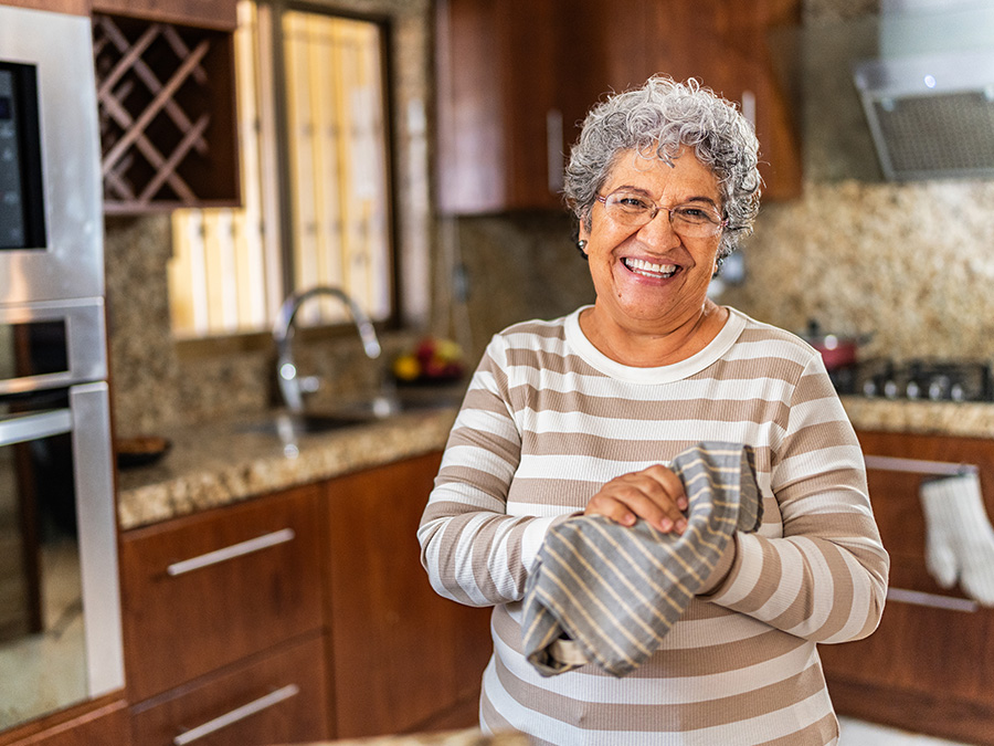 A woman stands in a kitchen facing the camera. She is smiling and holding a dish rag.