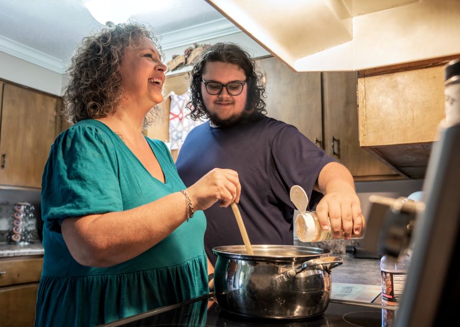 WoodmenLife member Angela Hunt and her son, Price, stand in their kitchen, in front of the stove. She is stirring the pot, and he is adding a seasoning.