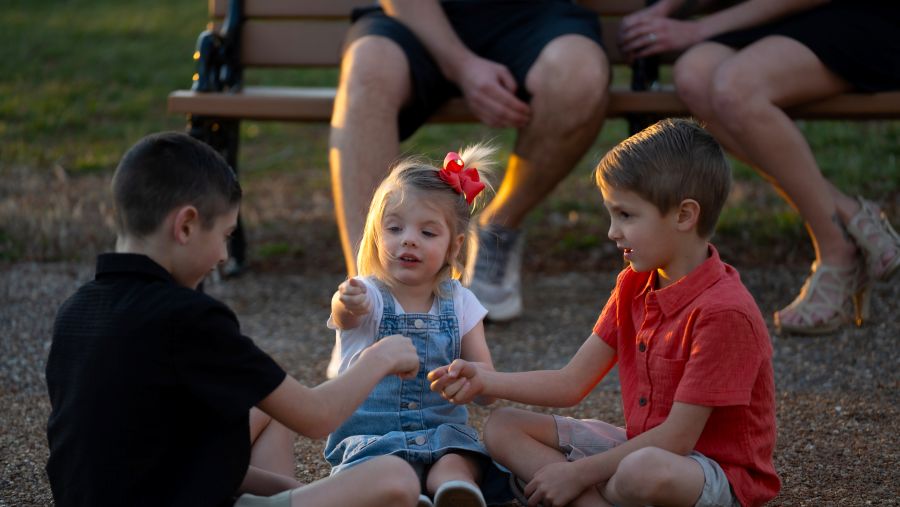Three kids — two boys and a girl — play together while sitting on the ground.