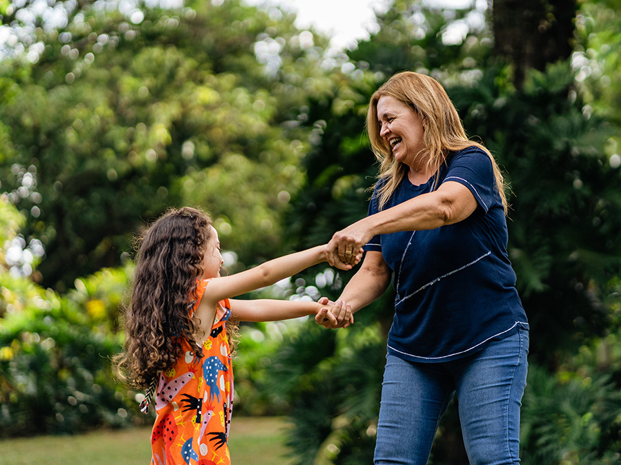 Stock photo shows an older woman and a young girl. They are standing outside, holding hands, and smiling. There are trees behind them.