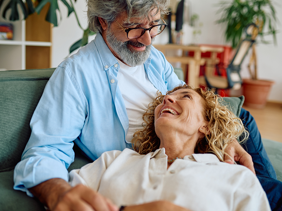 Stock photo shows a man sitting on a couch as a woman lays with her head in his lap. They are smiling at each other.