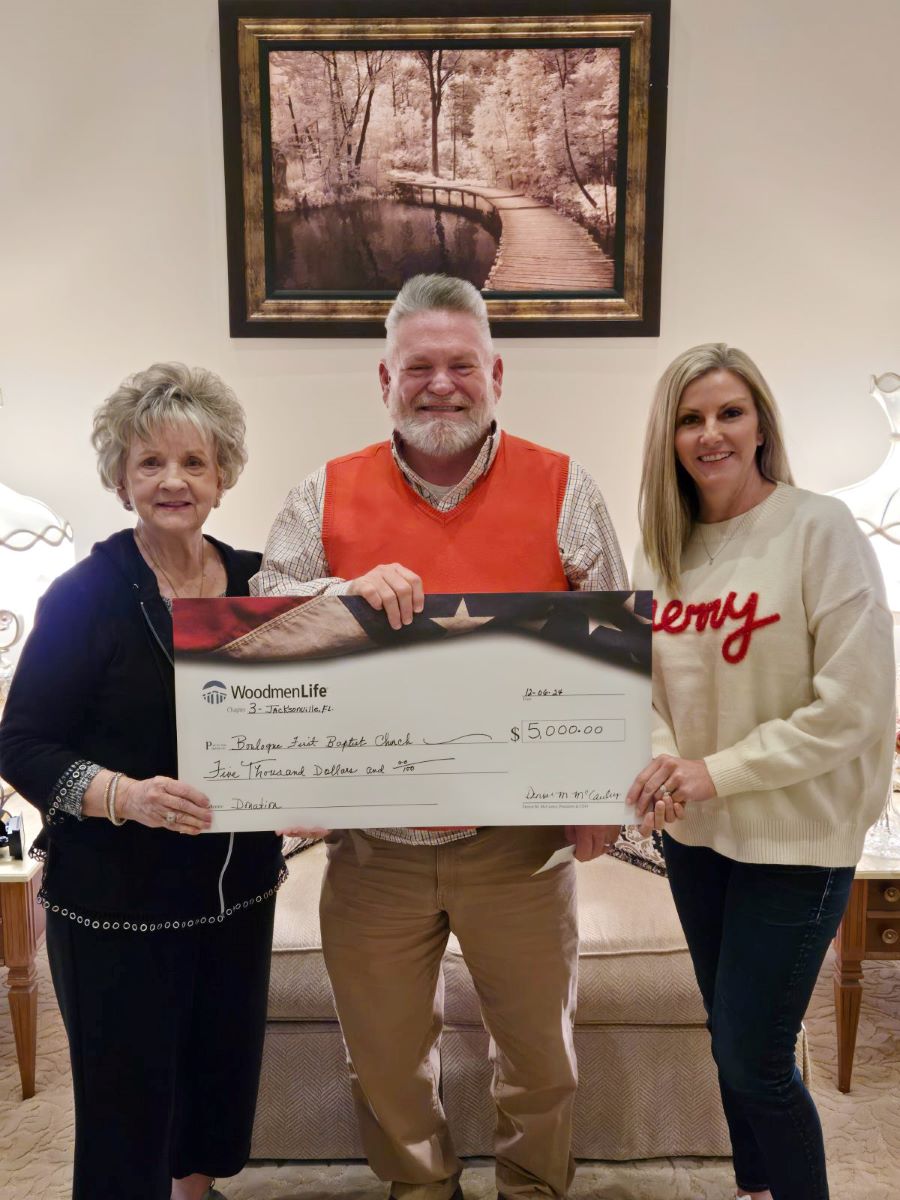 Three people stand with an oversized check. The WoodmenLife-branded check is made out to First Baptist Church of Boulougne in the amount of $5,000.