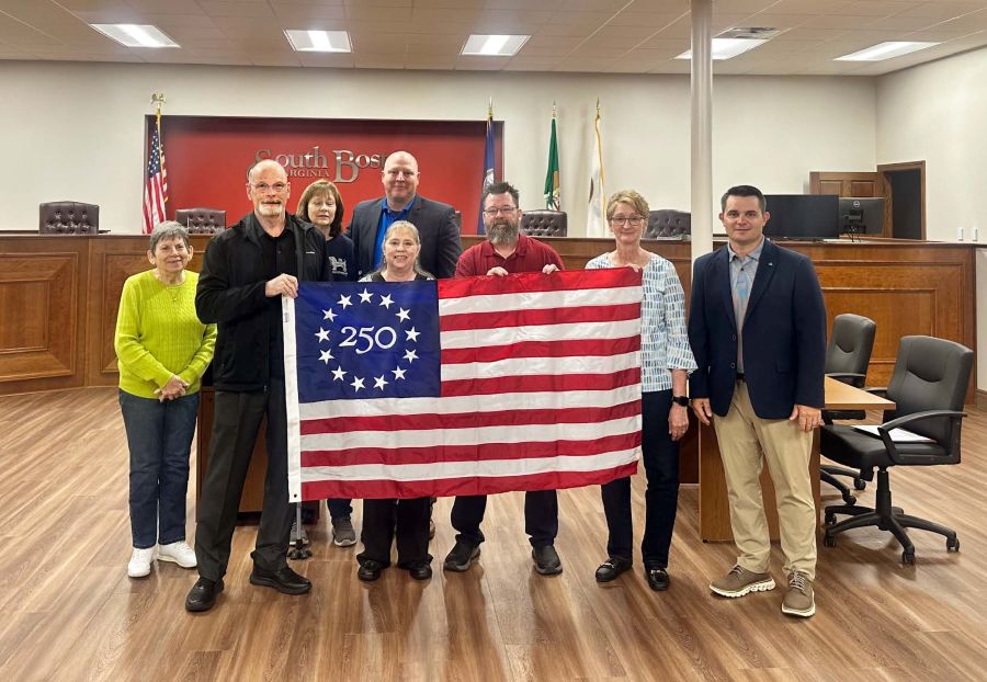 A group of eight people stand together holding a commemorative Betsy Ross 250 U.S. flag.