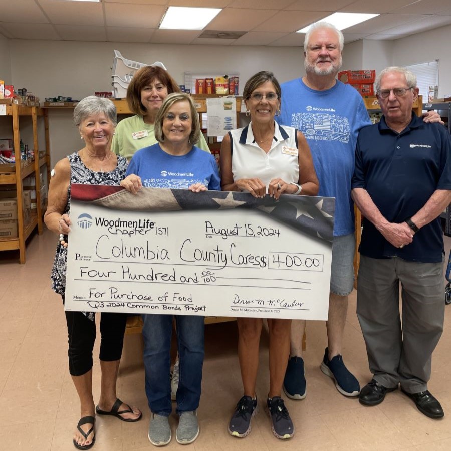 Six people stand together holding an oversized check. The check is for $400, made out to Columbia County Cares.