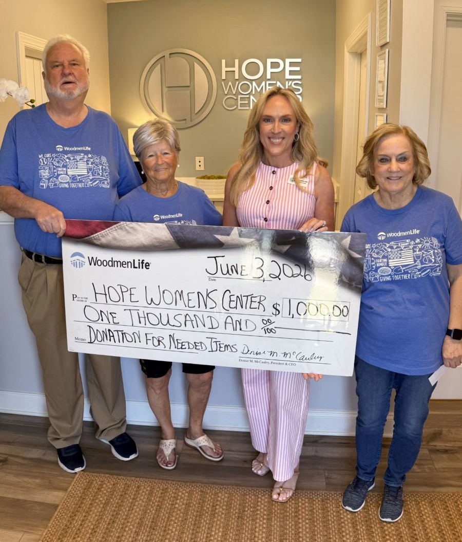 Photo shows four people standing together and holding an oversized check. The check is made out to the Hope Women's Center in the amount of $1,000. Behind them on the wall is the Hope Women's Center logo.