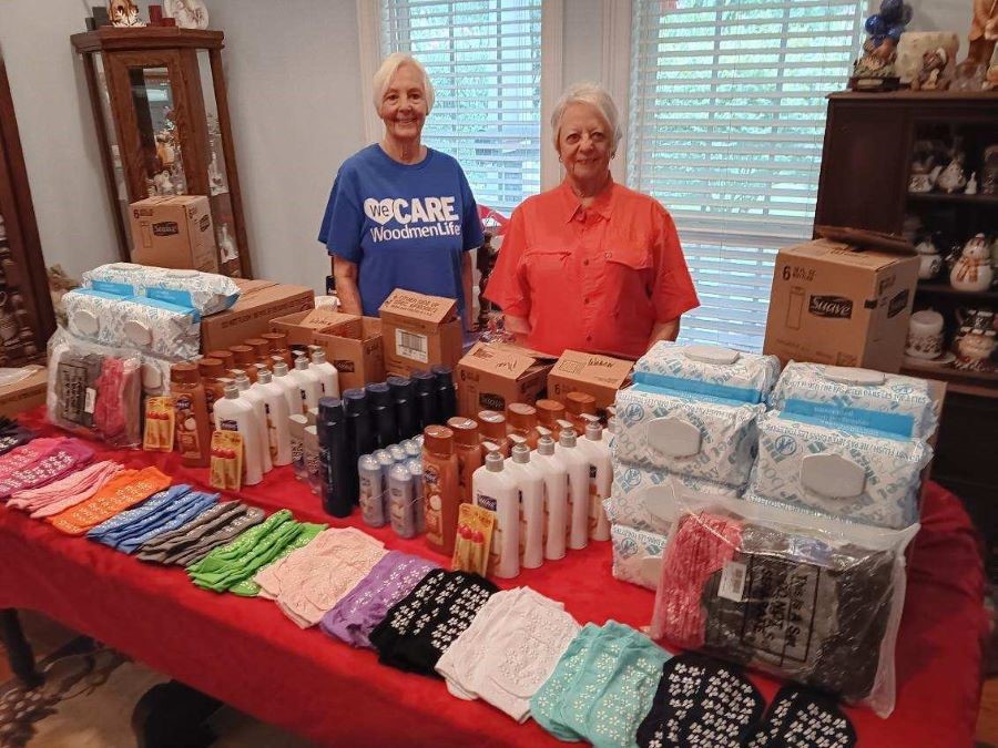 Two women stand behind a table filled with donated personal care items.