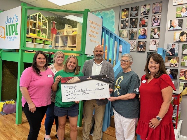 Six people stand together holding an oversized check. The check is made out to Jay's Hope Foundation in the amount of $5,000.