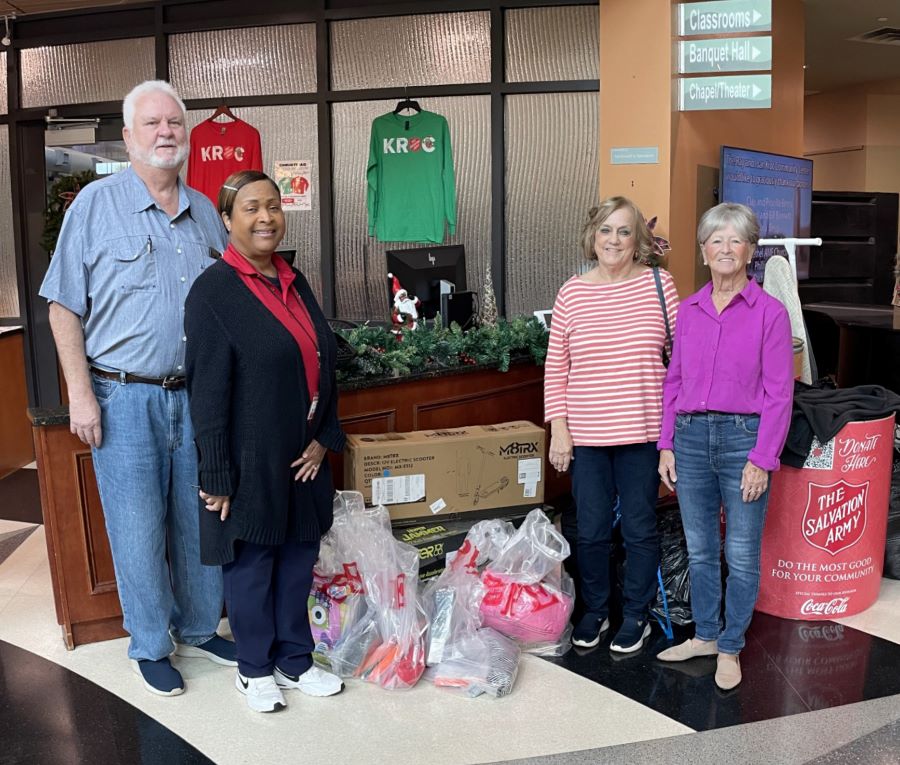 Four people stand beside several plastic bags full of donations. Behind them on the right side is a donation barrel with the Salvation Army logo on it.