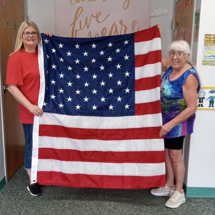 Two women stand together holding up an American flag.