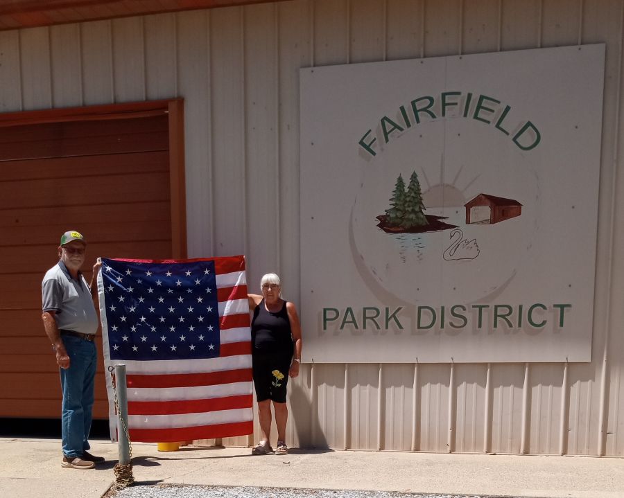 Photo shows two people holding a 5-foot-by-8-foot U.S. flag. On the building behind them is a large white sign that says "Fairfield Park District."