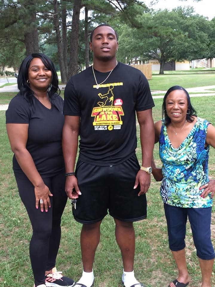 Photo shows three people: two women on either side of a young man. They are standing outside.