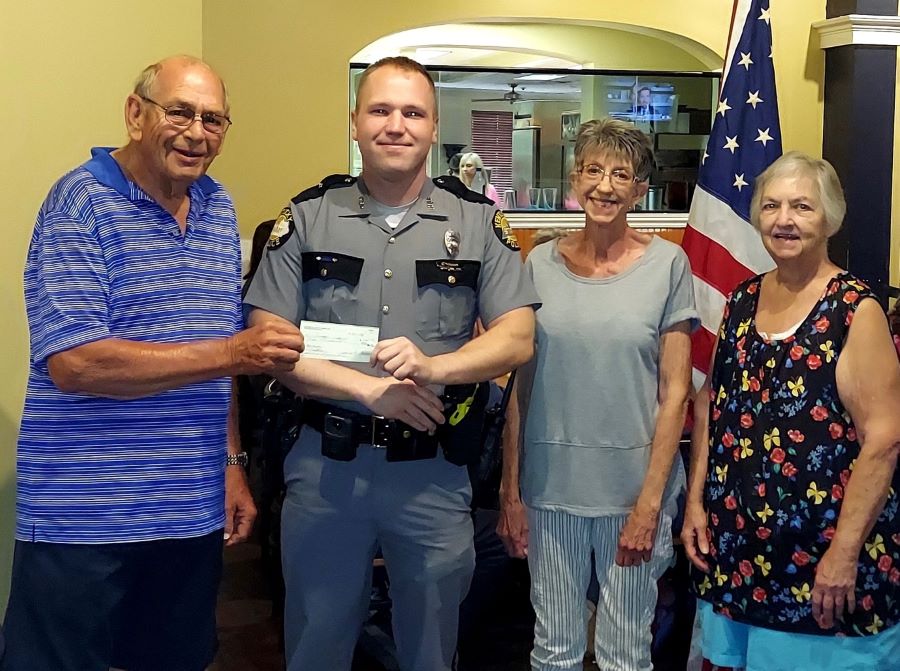 Two men and two women pose for this photo. One man is handing a check to the other man, who is wearing a law enforcement uniform.