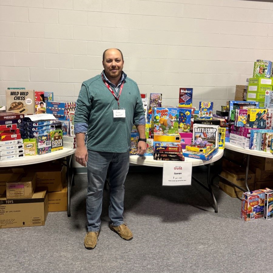 A man stands with tables filled with toys behind him.