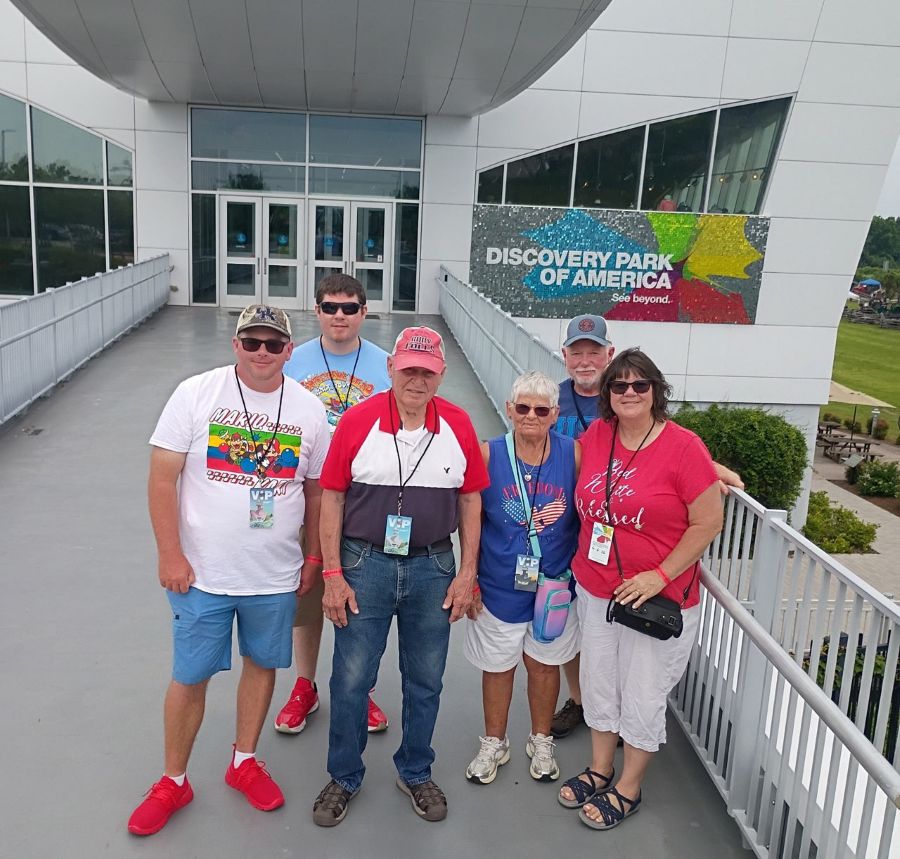 Photo shows six people standing together. They are standing on a walkway up to a building. A sign on the building says "Discover Park of America."