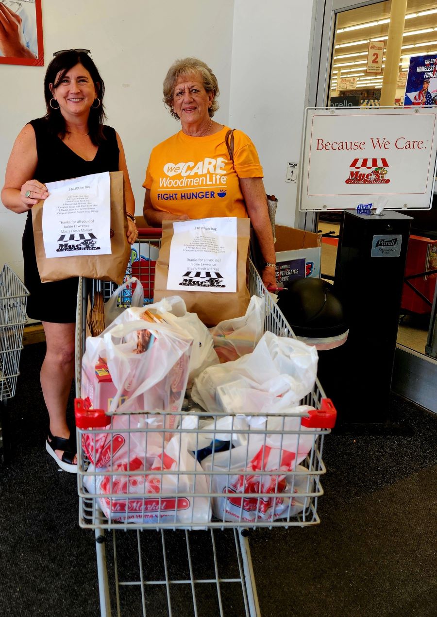 Two women stand with a grocery cart filled with bags of donated food.