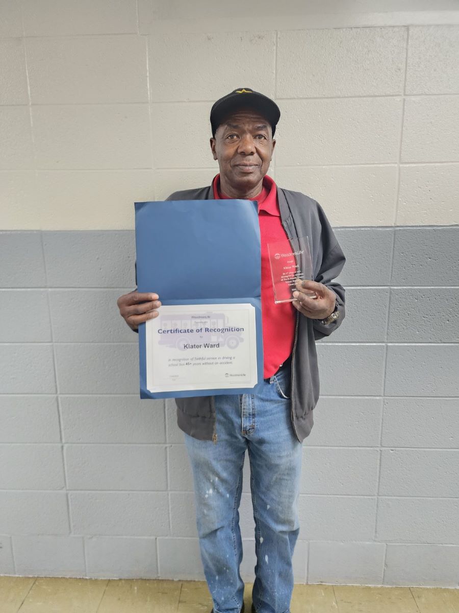 A man stands holding a certificate with his name and a glass award.