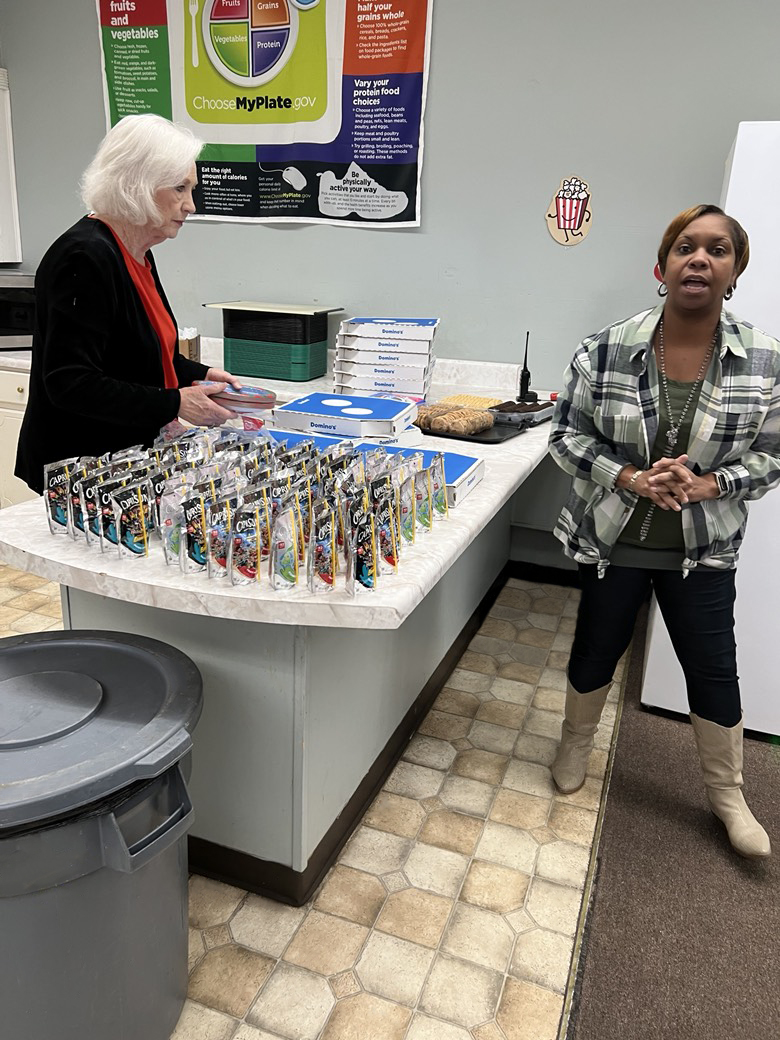 Two women appear in the photo. They are standing around a counter that has Domino's pizza, cookies, and Capri Sun on it.