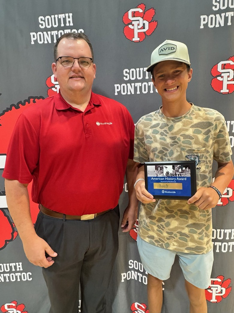 A man and a teenage boy stand together for the photo. The boy is holding a plaque that says "American History Award presented by WoodmenLife." Behind them is a backdrop with the South Pontotoc school logo.
