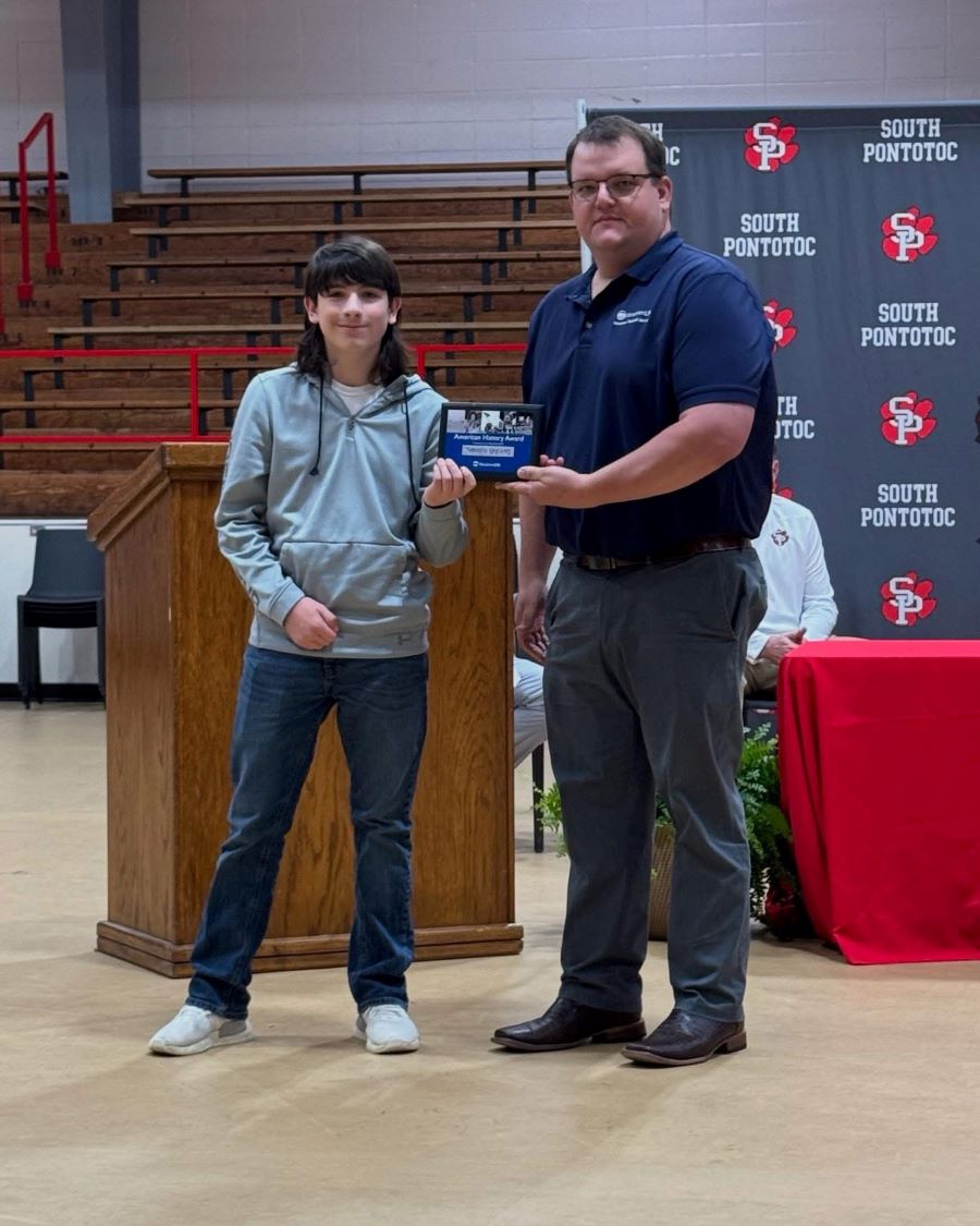A man is presenting a plaque to a student. Behind them is a podium and a backdrop that says "South Pontotoc."