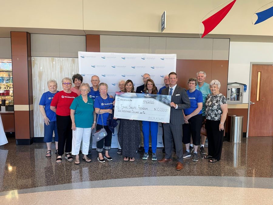 15 people stand together around an oversized WoodmenLife-branded check. The check, dated 9/4/2025, is made out to Final Salute Program in the amount of $10,000.