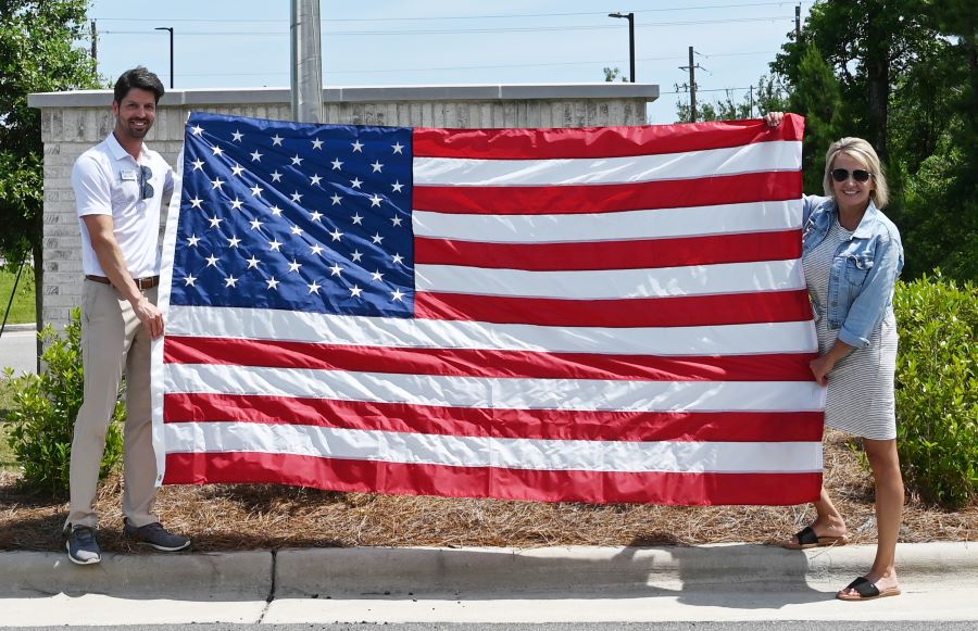 A man and a woman hold up a 5-by-8-foot American flag. They are standing outside.