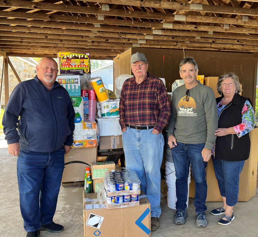 Four people stand with a pile of supplies — including canned food and paper towels — that will be delivered to people impacted by Hurricane Helene.