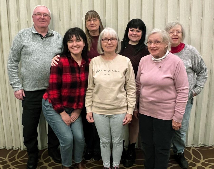 Seven people pose for the photo. Six of the people are women, and one is a man.