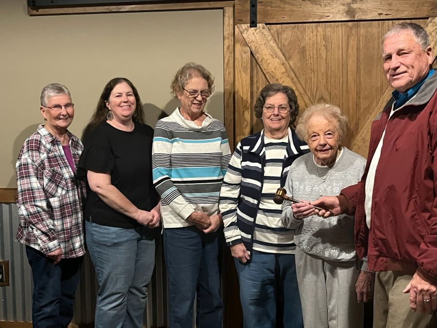 Six people stand together for a photo. The man on the far right is handing the woman next to him a small gavel.