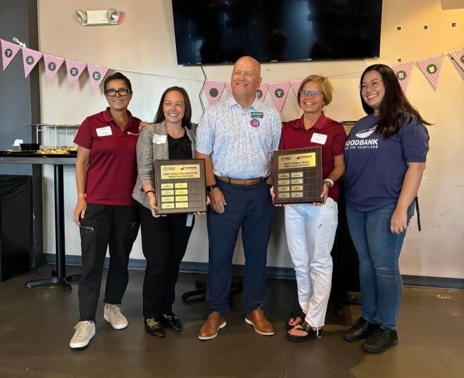 Five people stand together, two of whom are holding plaques. The plaques recognize WoodmenLife's success taking part in Strike Out Hunger month.