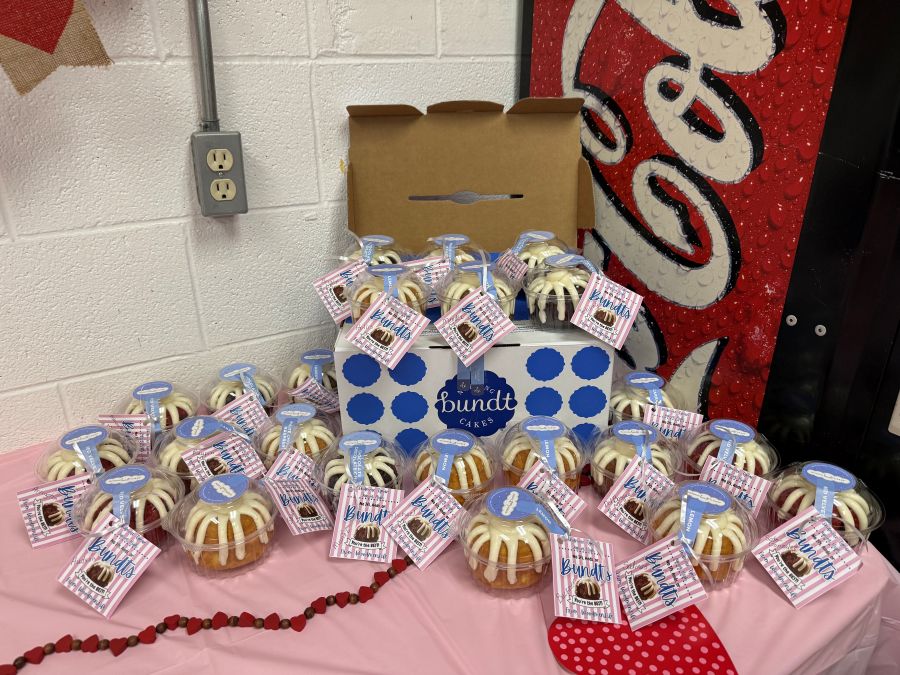Photo shows a table. On the table are about 25 individually packaged mini bundt cakes. Each has a tag on it.