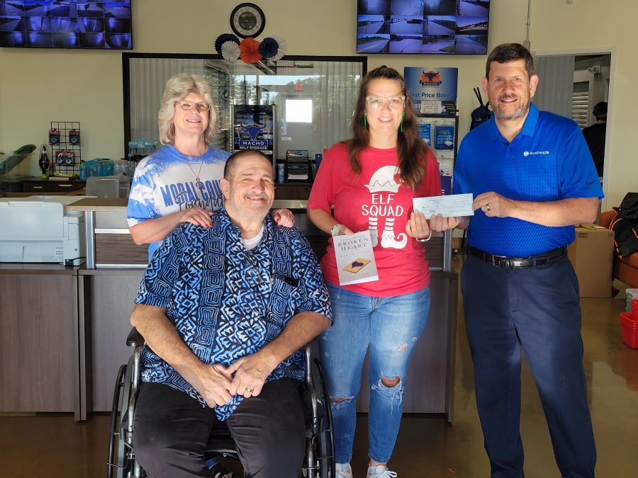 Four people pose for a picture. The person on the far right is handing over a check to the person next to him.