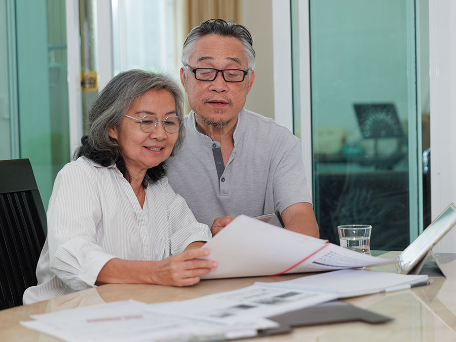 Stock photo shows an older man and woman sitting at a table. Together, they are looking over paperwork in front of them.