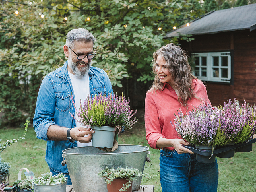 Stock image shows an older man and woman outside. They are both holding flower pots.