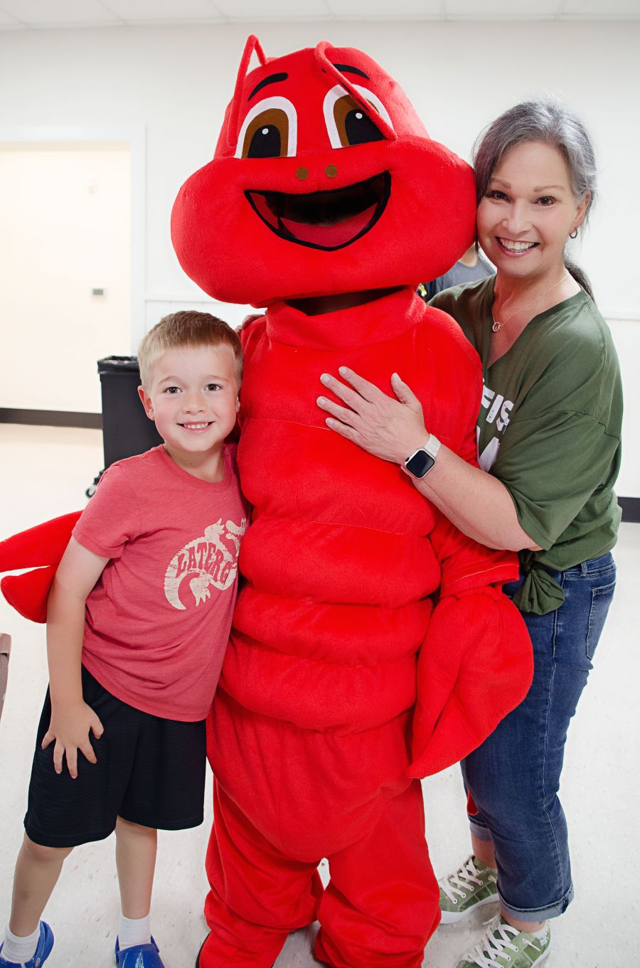 Photo shows a woman and a young boy posing with a person in a crawfish costume.