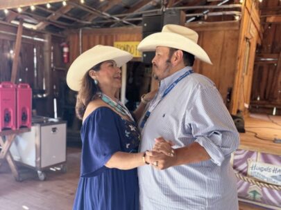 Photo shows a man and a woman dancing together. They are both wearing cowboy hats.
