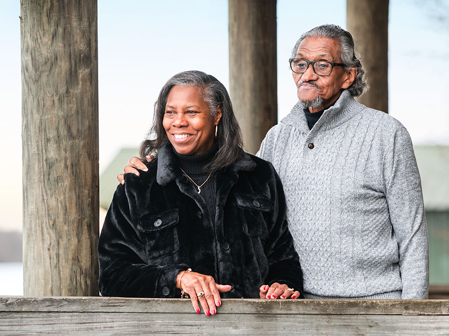 WoodmenLife member Bessie Pierce poses for a photo with her husband, William. She is wearing a black coat, and he is wearing a gray sweater. His arm is around her shoulder, and they are both looking off into the distance.