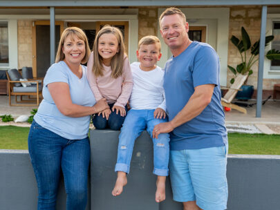 This stock image is of a family. The mom and dad are flanking two children, who are sitting on a waist-high wall.