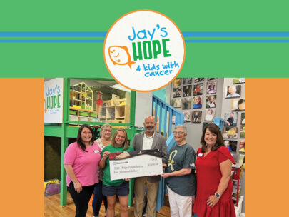 Image includes a photo of a check presentation. there are six people gathered around an oversized check, which is made out to Jay's Hope Foundation in the amount of $5,000. Surrounding the photo is a green, orange and blue border and the Jay's Hope Foundation logo.