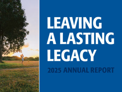Image has a wide blue bar with the text "Leaving a Lasting Legacy, 2025 Annual Report." Along the left side of the image is a stock photo of a woman holding a child; they are standing outdoors in a grassy area, with a tree next to them and the sun behind them.