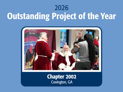 Graphic says "2026 Outstanding Project of the Year" across the top, and "Chapter 2002, Covington, GA" across the bottom. In the middle is a photo of man carrying a small child up to see people dressed as Santa Claus and Mrs. Claus. The background of the graphic is a medium blue.