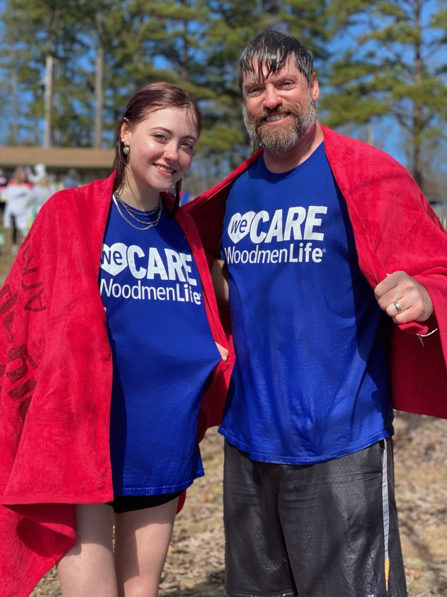 A man and his daughter stand together for the photo. They are both soaking wet and wearing blue WoodmenLife T-shirts.