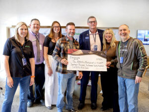 Photo shows seven people standing with an oversized WoodmenLife-branded check. The check is made out to the Arthritis Foundation in the amount of $17,625.