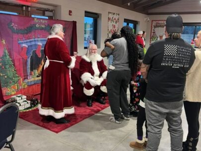 Photo shows a line of kids and their parents waiting to meet Santa and Mrs. Claus.