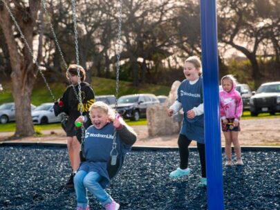 Photo shows children playing on a swing set. Two of the children are wearing WoodmenLife T-shirts.