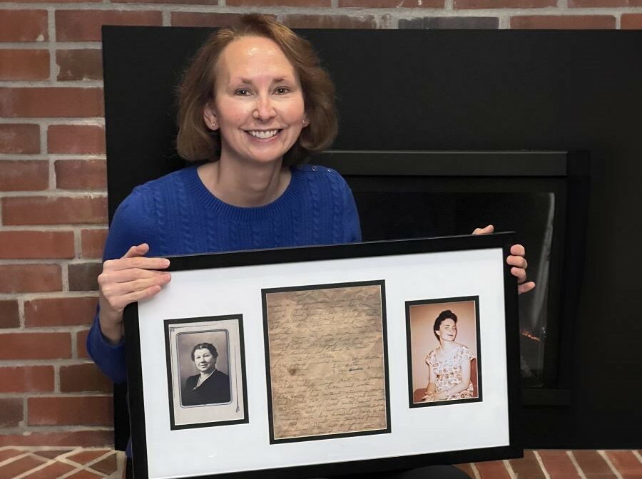 WoodmenLife President & CEO Denise McCauley sits in front of a fireplace, holding a framed picture on her lap. At the center of the framed picture is the recipe for Chocolate Popcorn; the paper has browned with age. One either side of the recipe is a photo, one of McCauley's mom and one of her mom's grandma.