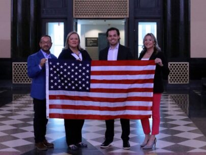 Four people stand together holding a 3-foot-by-5-foot American flag.