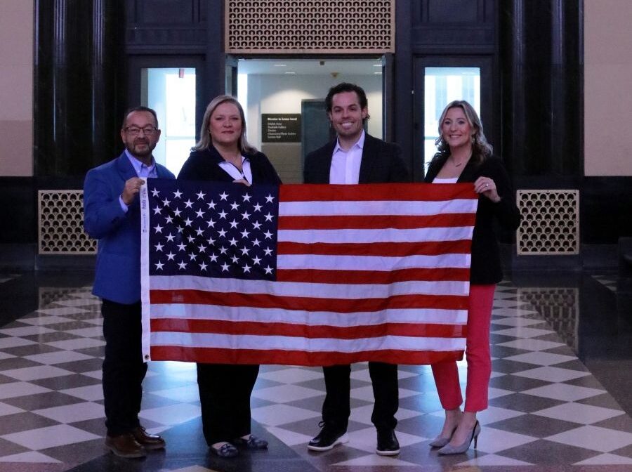 Four people stand together holding a 3-foot-by-5-foot American flag.