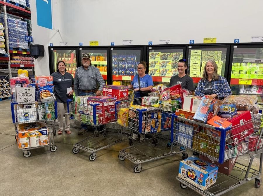 Photo shows five people standing in a store with four full shopping carts. In the carts are a wide variety of food, boxes of diapers, paper towels, and laundry detergent.