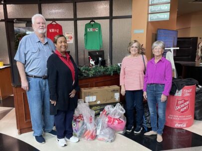 Four people stand several plastic bags full of donations. Behind them on the right side is a donation barrel with the Salvation Army logo on it.